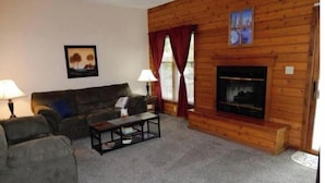 A cozy living room with a fireplace, a sofa, a coffee table, and two lamps. - Poconos Dream House (East Stroudsburg)