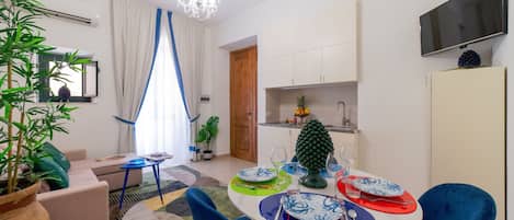 Een moderne woonkamer met een bank, een eettafel voor vier personen, en een keuken met een televisie en kasten.