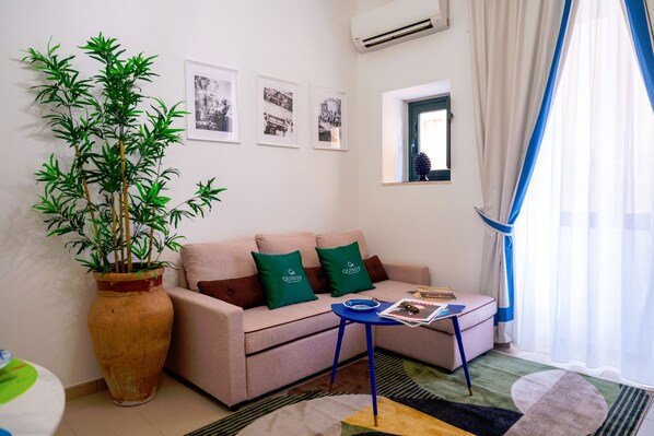 A living room with a sofa, a coffee table, a large potted plant, and framed pictures on the wall.