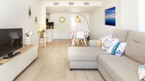 A modern living room with a flat-screen TV, a sofa, a dining area with a table and chairs, and a kitchen in the background. - El Fenua by Interhome (St Antoni de Calonge)