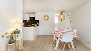 A modern dining area with a white table set for four, a kitchen in the background, and a decorative mirror on the wall. - El Fenua by Interhome (St Antoni de Calonge)