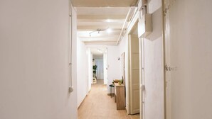 Een smalle gang met witte wanden en houten vloeren, leidend naar een kamer met een deur aan de rechterkant.