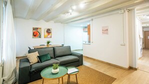 Een moderne woonkamer met een grijze bank, een klein bijzettafeltje met een plant, en een eethoek met een tafel en stoelen.
