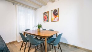 Een eetgedeelte met een houten tafel en zes stoelen, een potplant en twee abstracte schilderijen aan de muur.