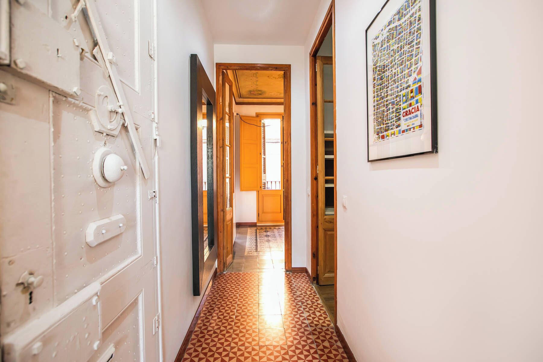 A hallway with a patterned floor, a door with a handle, and a framed picture on the wall.