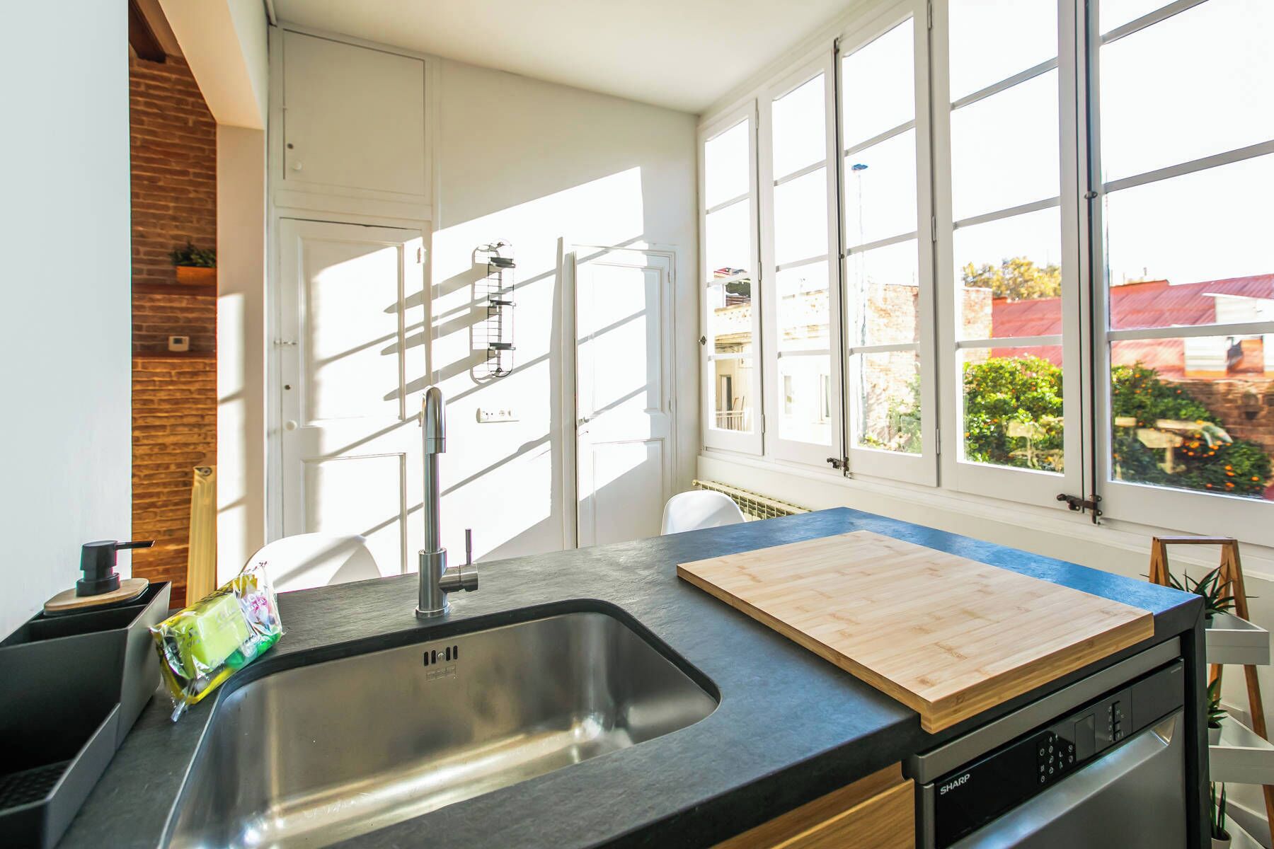 A modern kitchen with a large sink, wooden countertop, and a view of the city through large windows.