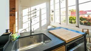 A modern kitchen with a large sink, wooden countertop, and a view of the city through large windows.