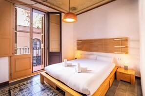 Un dormitorio con cama, mesitas de noche, lámpara colgante y vista a través de una puerta abierta.