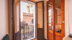 A room with a sliding glass door leading to a balcony, a wooden door, and a small window with a mesh screen.