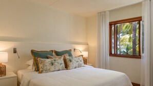 Habitación de hotel con una cama, dos mesitas de noche, una ventana con cortinas y vistas a palmeras.