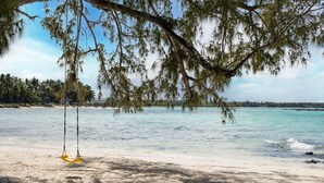 Una playa con una silla hamaca, agua turquesa cristalina y palmeras al fondo.