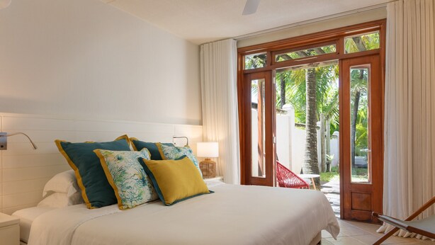 A bedroom with a bed, pillows, a nightstand, a lamp, and a view of the outdoors through a glass door.