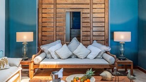 A room with a wooden staircase, a sofa with cushions, a dining table with a fruit bowl, and two lamps.