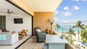 A balcony with a view of the beach, a sofa, a chair, a table, and potted plants. - Manta Morada: Mar, San Pancho, Beachfront and Ocean views (San Francisco)