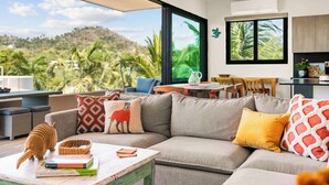 A modern living room with a large sofa, a coffee table, and a view of a lush landscape. - Manta Morada: Mar, San Pancho, Beachfront and Ocean views (San Francisco)