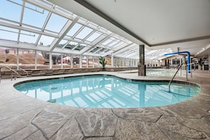 Una piscina interior con techo de cristal, suelo de piedra y vistas al exterior.