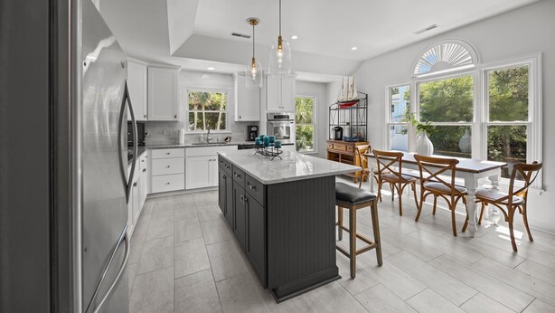 A modern kitchen with white cabinets, a central island, and a dining area with wooden chairs. - Modern Beach Home on Quiet Street w/Private Pool. 1 Block to Beach! (Isle Of Palms)
