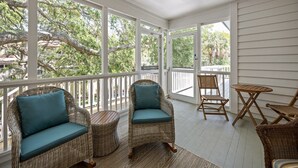 A covered porch with wicker furniture, including two chairs with teal cushions and a small table. - Modern Beach Home on Quiet Street w/Private Pool. 1 Block to Beach! (Isle Of Palms)