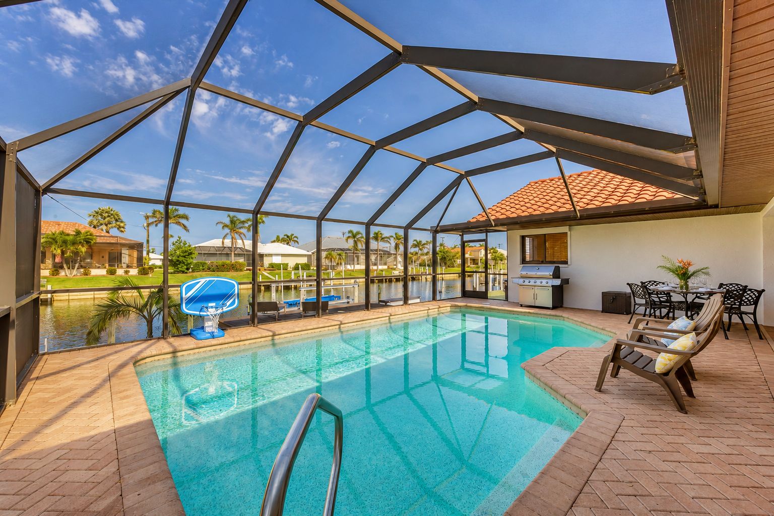 An indoor swimming pool with a glass ceiling, surrounded by lounge chairs and a barbecue area.