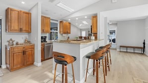 Een moderne keuken met houten kasten, een centraal eiland met barkrukken en een uitzicht op de eetruimte.