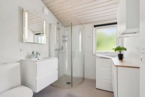 A modern bathroom with a glass-enclosed shower, a sink with a mirror, and a window.