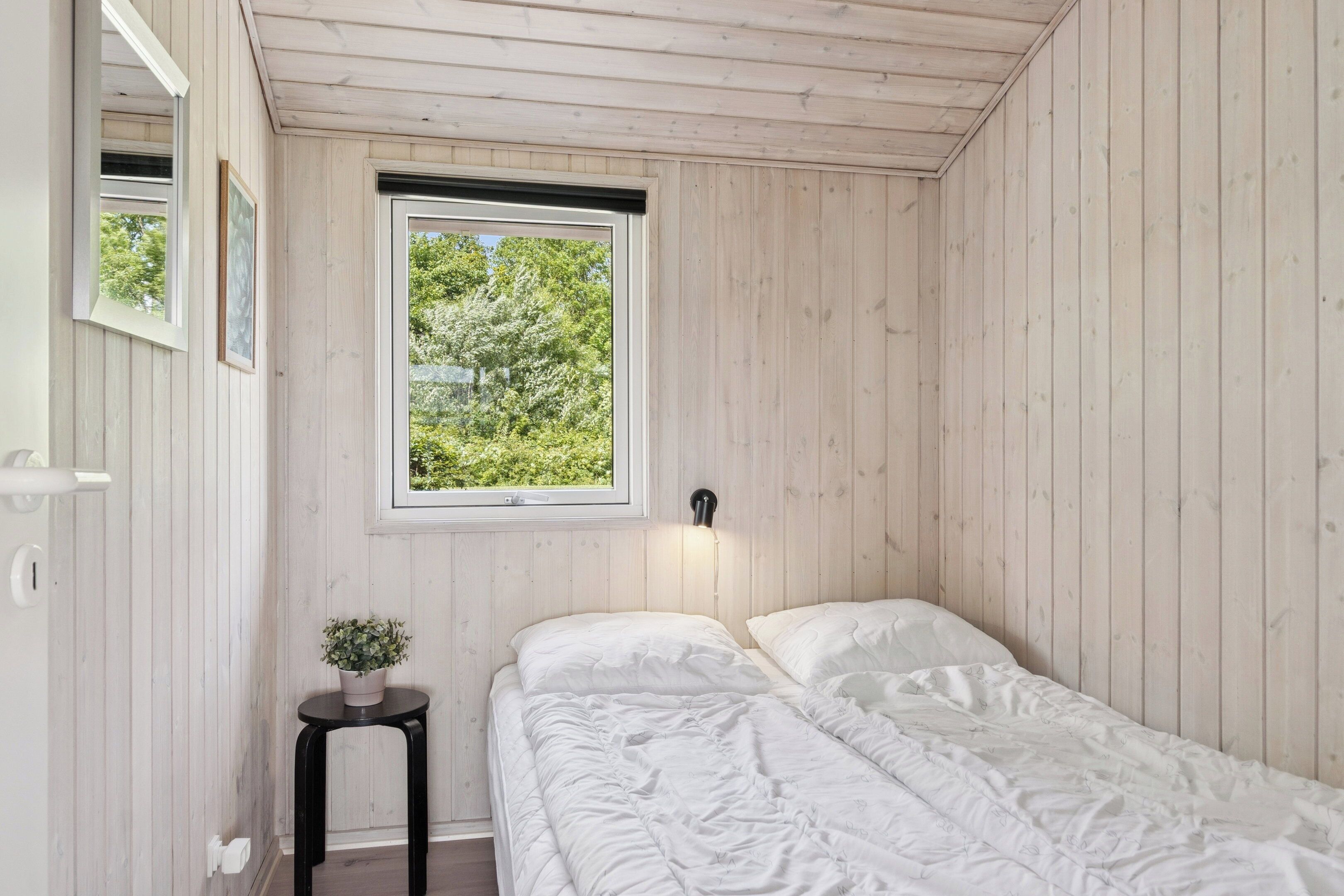 Ein Schlafzimmer mit einem Einzelbett, einem kleinen Tisch mit einer Pflanze, einem Fenster mit Blick auf Grünflächen und Holzwänden.