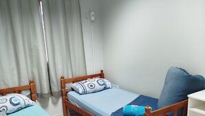 A small, tidy room with two wooden beds, each with blue bedding and pillows. There is a white desk with a chair and a small trash bin. - Pousada Central  (Joinville)