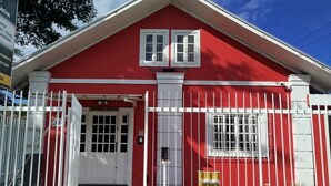 A red building with a white door and window, surrounded by a white fence. - Pousada Central  (Joinville)