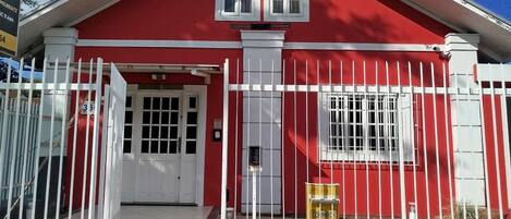 A red building with a white door and window, surrounded by a white fence.