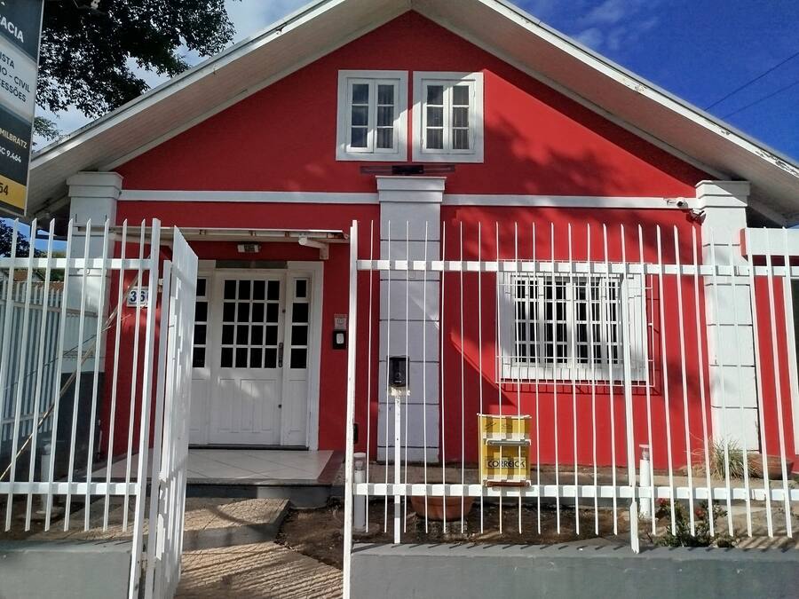 Un edificio rojo con puerta y ventana blancas, rodeado por una valla blanca.