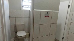 A small, tiled bathroom with a toilet, a shower stall, and a window. - Pousada Central  (Joinville)