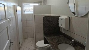 A small, compact bathroom with a toilet, sink, and mirror. - Pousada Central  (Joinville)