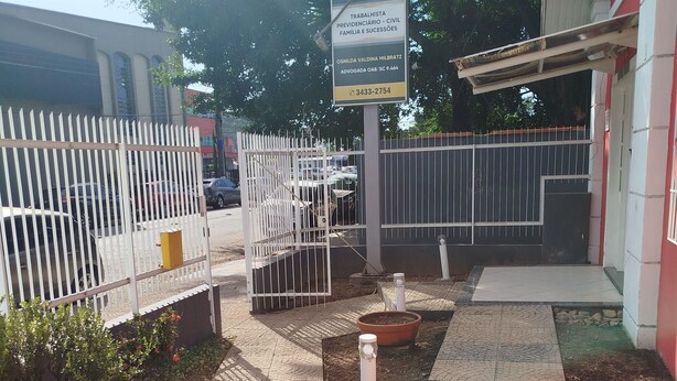 A paved courtyard with a white fence, a signboard, and a potted plant. - Pousada Central  (Joinville)