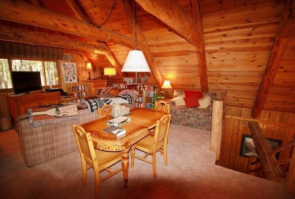A cozy cabin interior with a wooden dining table, chairs, a sofa, and a television. - Lodge on Wiltbank St (Greer)