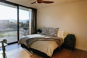 A bedroom with a large window, a bed, a nightstand, and a ceiling fan. - Ridgecrest - Lake Views - Sleeps 12 (Wanaka)