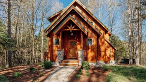 A wooden cabin with a stone foundation, a front porch, and a clear path leading to the entrance.