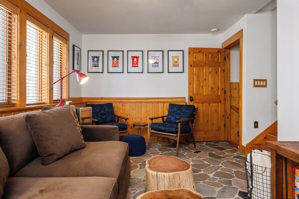 Una habitación acogedora con un sofá marrón, dos sillas azules, una lámpara de pie roja y una puerta de madera.