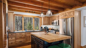 A kitchen with wooden cabinets, a large island, stainless steel appliances, and green stools.