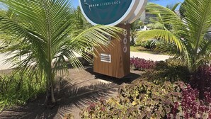 Schild für Makia Beach Experience mit Palmen und bunten Pflanzen im Vordergrund.