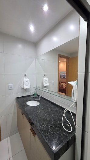 Une salle de bain moderne avec un plan de toilette en granit noir, un lavabo blanc et une cabine de douche en verre.