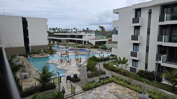 Ein modernes Hotel mit einem zentral gelegenen Poolbereich, umgeben von üppiger Bepflanzung und zahlreichen Balkonen.