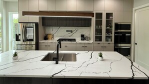 Een moderne keuken met een marmeren aanrechtblad, ingebouwde apparatuur en een groot eiland met een spoelbak.