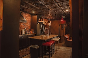 A kitchen with a brick wall, a stainless steel refrigerator, and a wooden countertop.