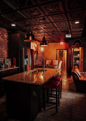 A bar area with a central island, stools, a refrigerator, and a brick wall.