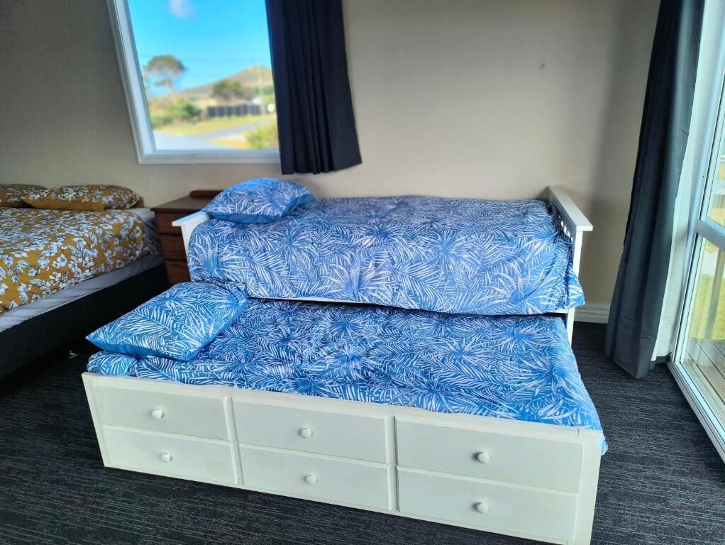 A room with a bed, a small white dresser, and a window with a view of a landscape.