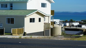 A two-story house with a curved roof, a fenced yard, and a view of the sea and mountains in the background.