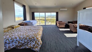 A hotel room with a large bed, a sofa, a chair, and a balcony with a view.