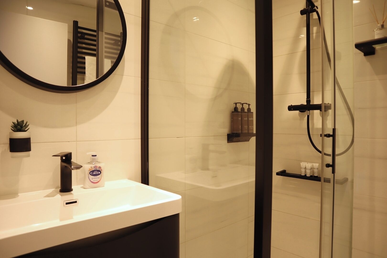 A modern bathroom with a round mirror, a white sink, and a glass-enclosed shower area.