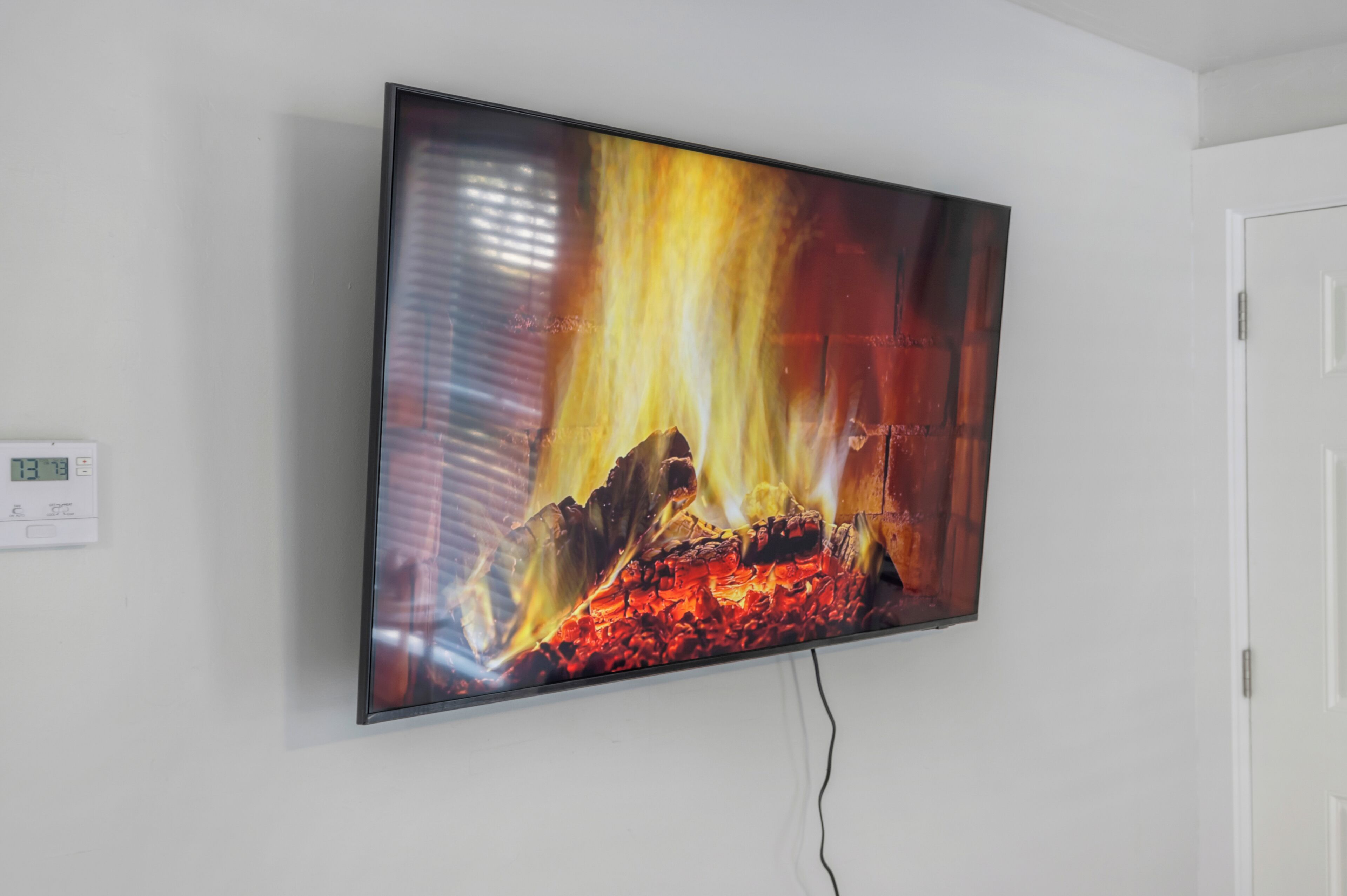 A flat-screen TV mounted on a white wall displaying a fireplace scene.