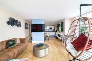 Ein modernes Wohnzimmer mit einer Couch, einem Hängesessel, einem Couchtisch und einem an der Wand befestigten Flachbildfernseher.